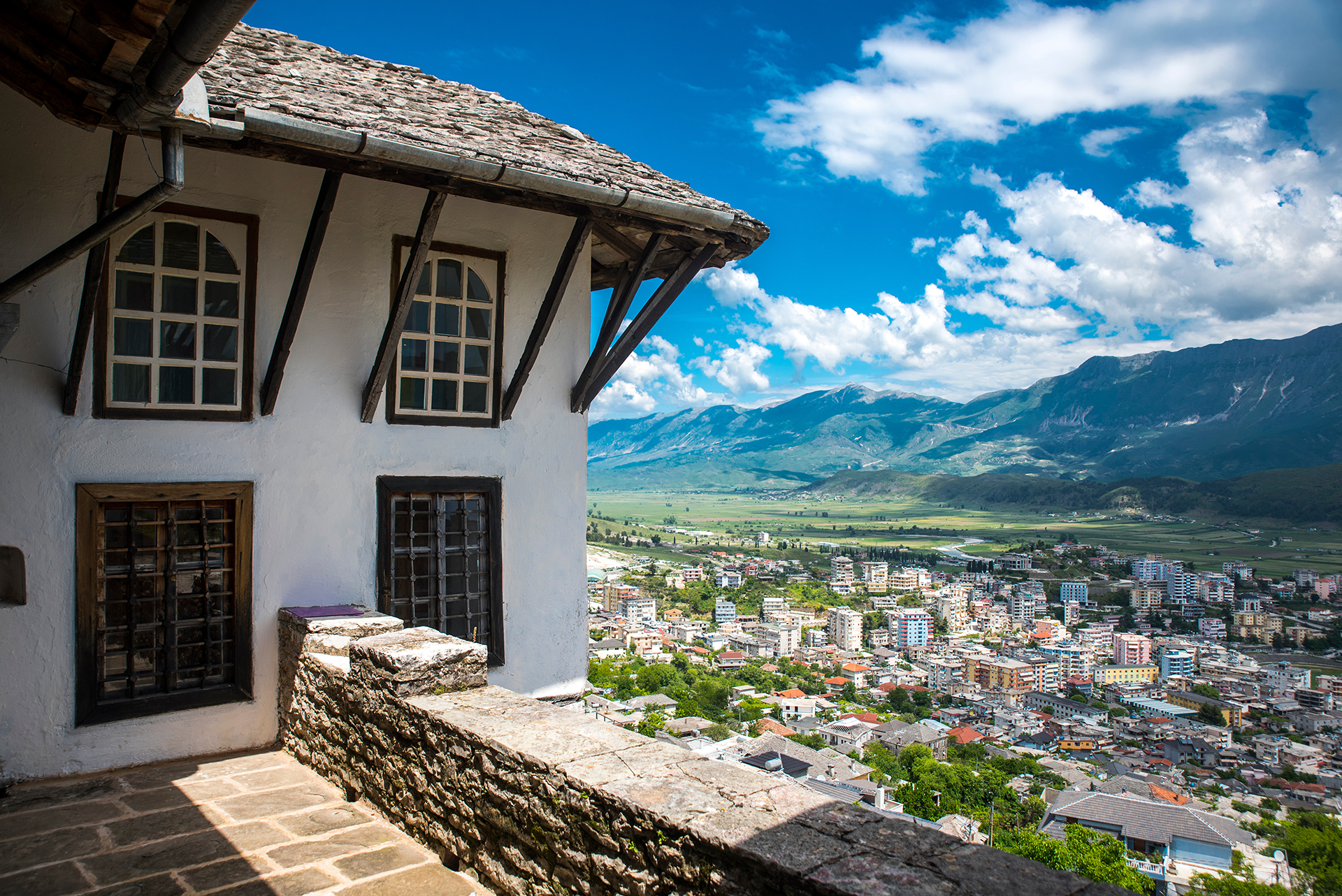 Traditional white stone house with wooden beams overlooking a valley town and mountains under a bright blue sky, representing a 7-day journey through UNESCO-protected heritage sites.
